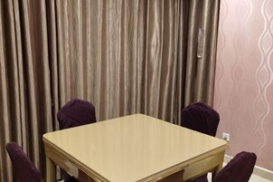 Una habitación con una mesa de madera y cuatro sillas moradas, una cortina y un papel tapiz estampado.