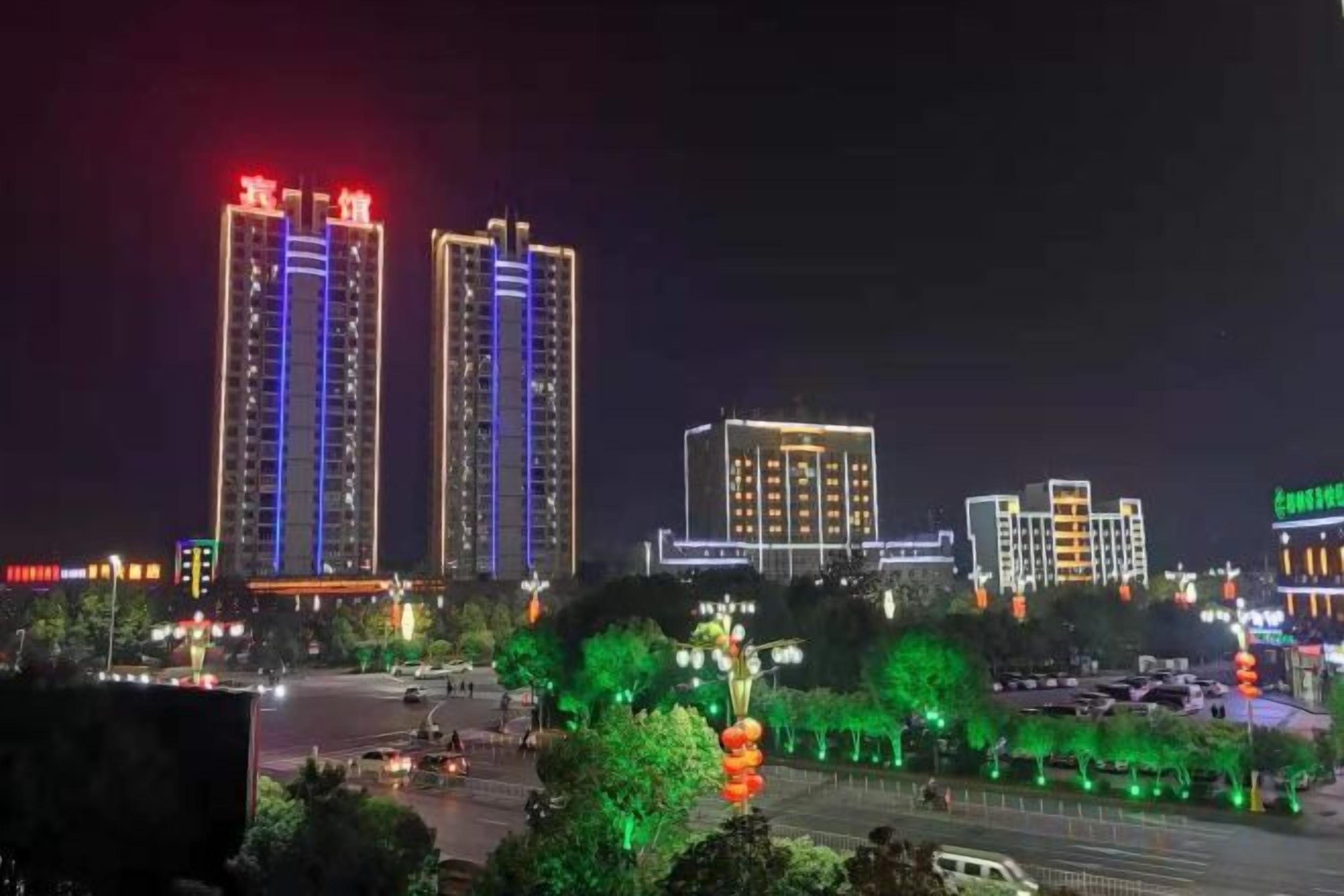A nighttime cityscape with illuminated high-rise buildings and a well-lit street.