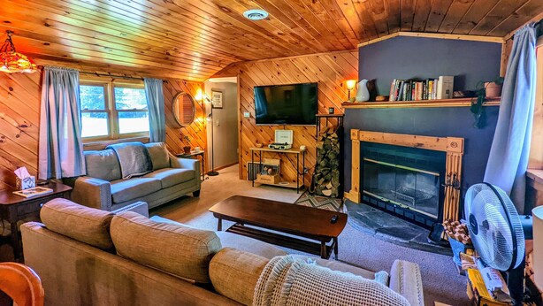 A cozy cabin interior with a wooden ceiling, a fireplace, a sofa, a television, and a fan. - Your Sunny Bungalow Awaits! (Big Indian)