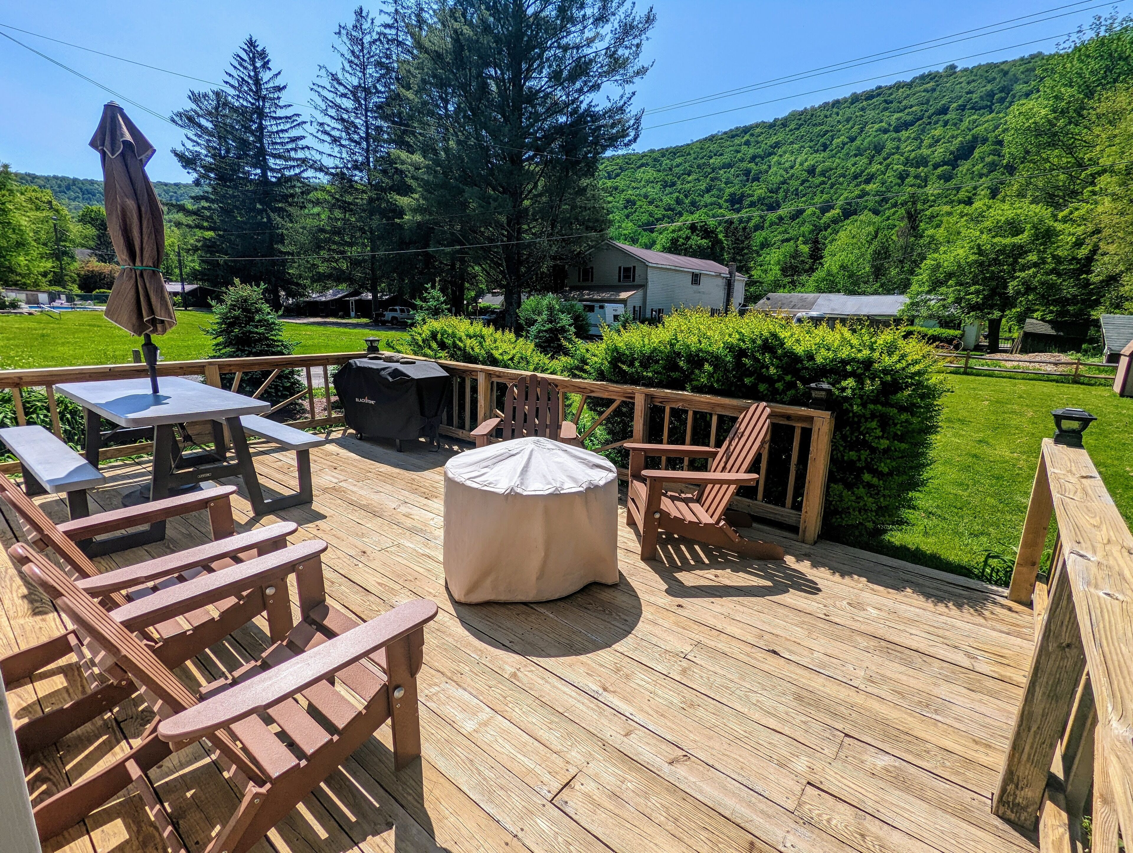 Une terrasse en bois aménagée avec du mobilier d’extérieur, notamment une table et des chaises, ainsi qu’un barbecue.