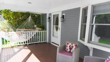A covered porch with a hammock, wicker chairs, and a door with a glass panel.
