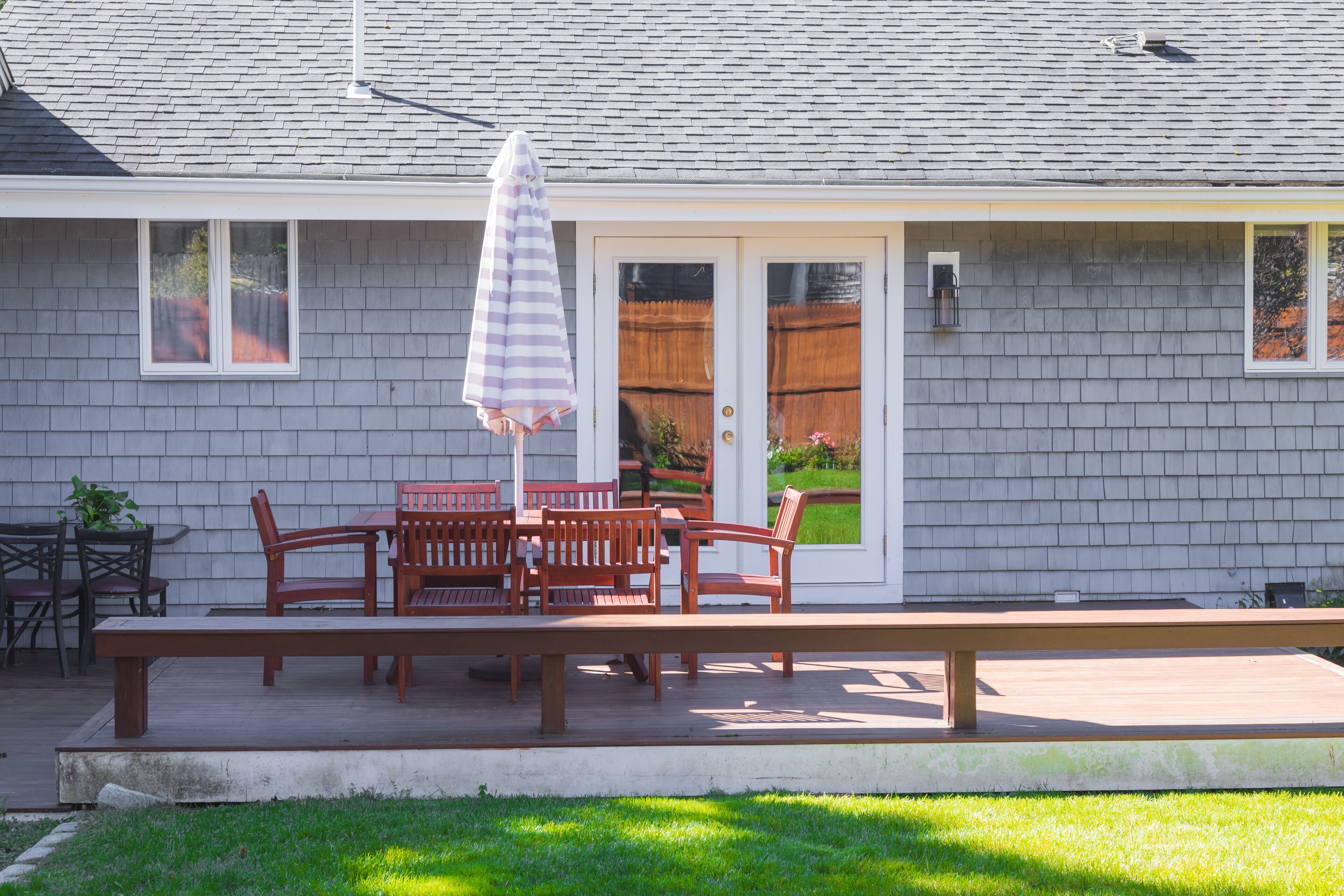 Une terrasse avec une table et des chaises en bois, un banc et un parasol à rayures.
