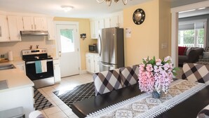 A modern kitchen with white cabinets, a stainless steel refrigerator, and a dining area with a patterned tablecloth and a vase of flowers. - Relax by Oak Bluffs Harbor, enjoy your 3-bedroom East Chip retreat (Oak Bluffs)