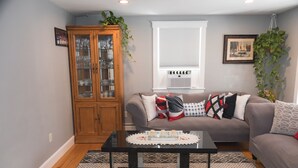 A living room with a brown sofa, a glass cabinet, a black coffee table, and patterned rugs. - Relax by Oak Bluffs Harbor, enjoy your 3-bedroom East Chip retreat (Oak Bluffs)