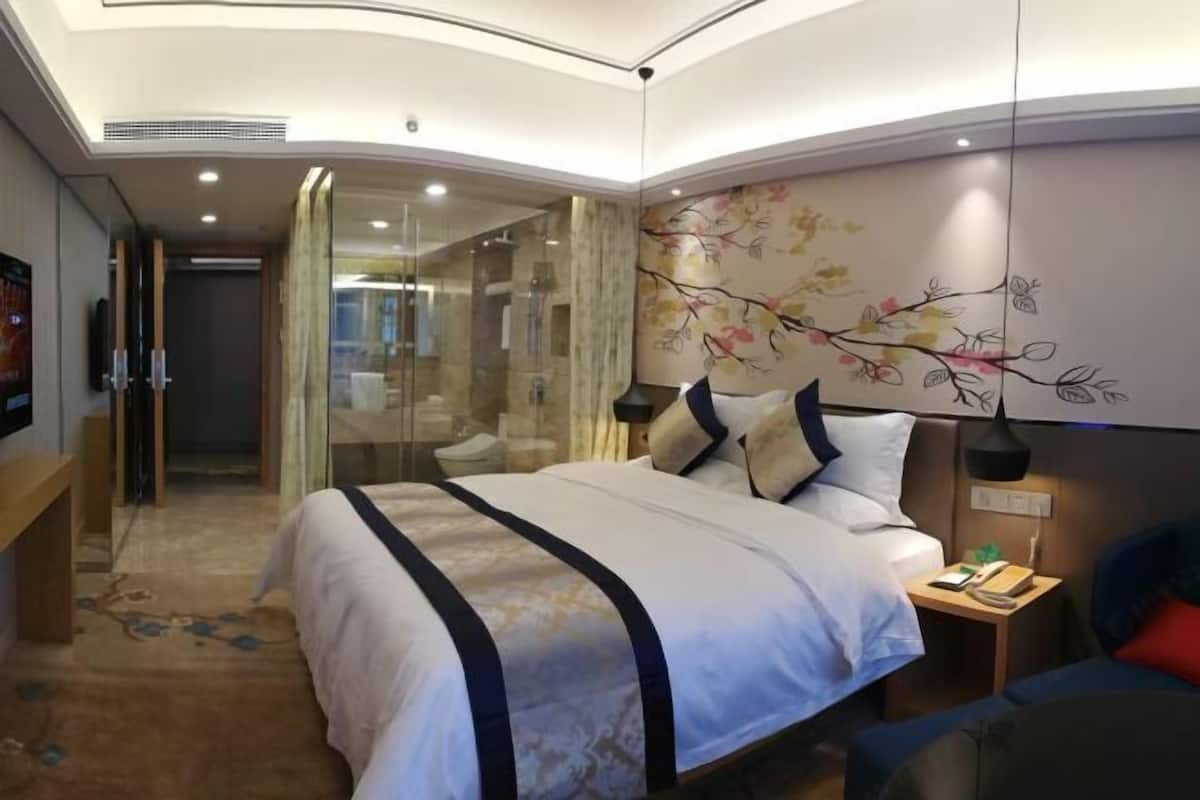 A hotel room with a large bed, a bedside table with a lamp, a TV, and a glass shower enclosure.
