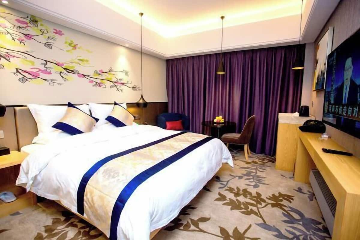 A hotel room with a large bed, a desk, a chair, a TV, and a purple curtain.