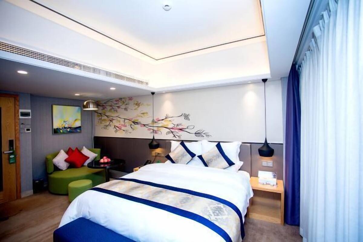 A modern hotel room with a large bed, a green sofa, and a decorative wall mural.
