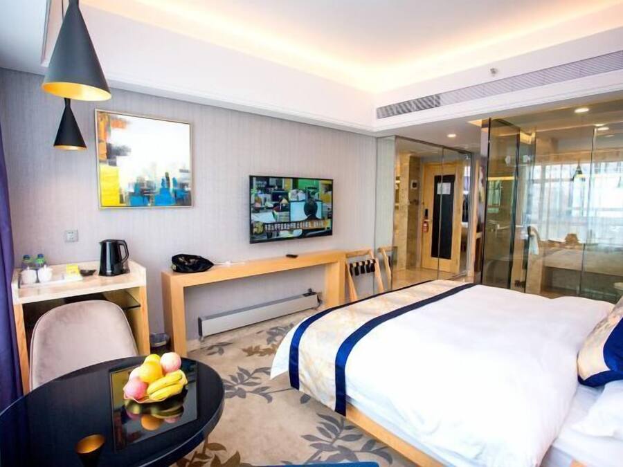 A hotel room with a bed, a desk with a computer, a TV, and a glass door leading to a balcony.