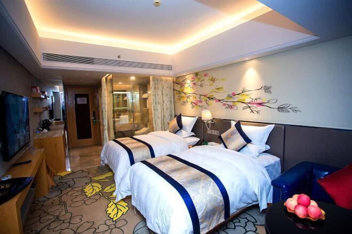 A hotel room with two beds, a TV, and a fruit bowl.