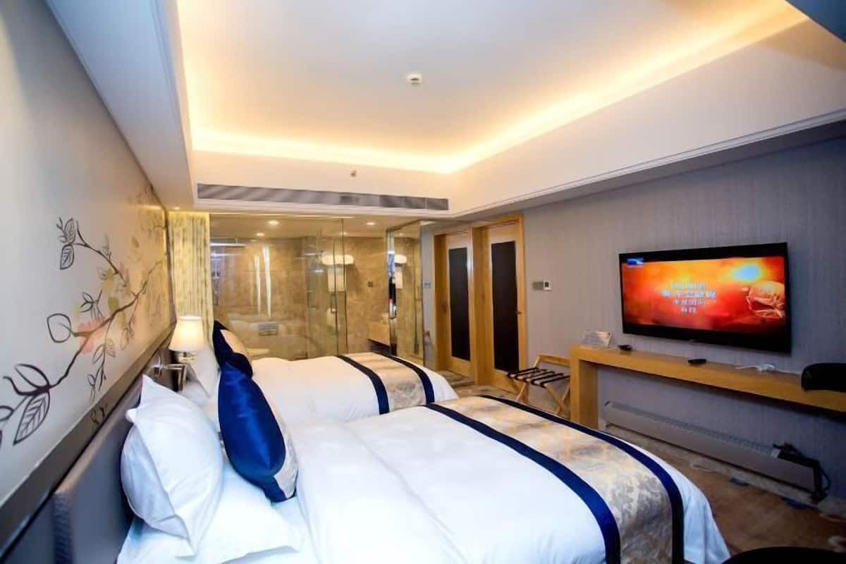 A hotel room with two beds, a TV, and a glass-enclosed shower area.