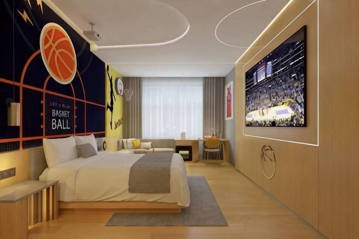 A modern hotel room with a large bed, a TV, a basketball-themed wall, and a desk.