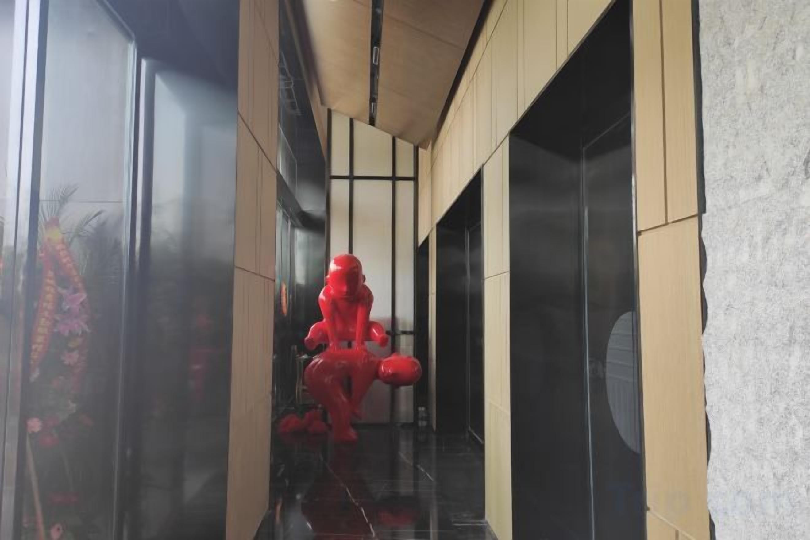 Um corredor com uma estátua vermelha, uma porta de vidro e uma parede de madeira.