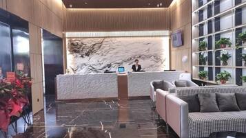 A hotel reception area with a marble wall, a reception desk, a sofa, and a plant wall.