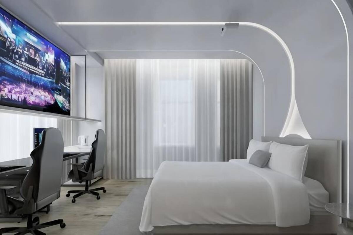 A modern hotel room with a bed, desk, chair, and a TV mounted on the wall.