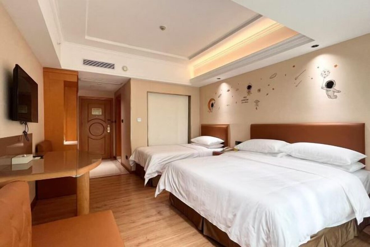 A hotel room with two beds, a desk, a TV, and a door leading to another room.