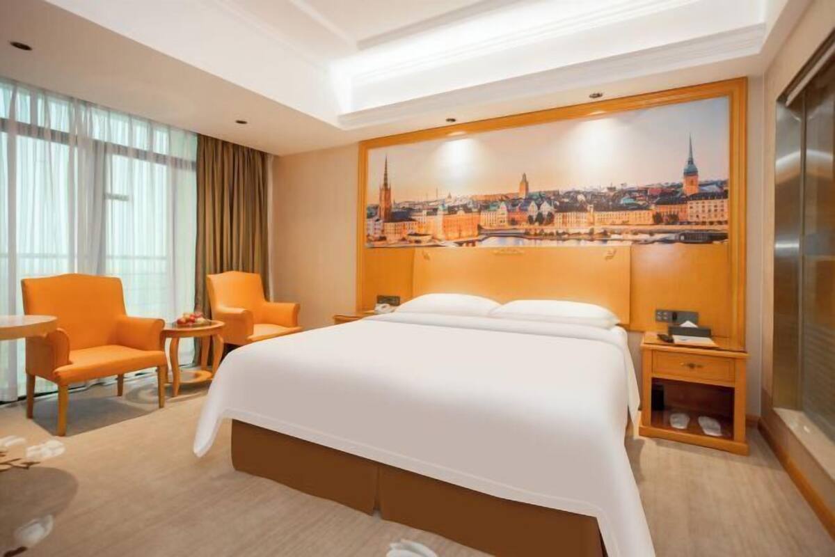 A hotel room with a large bed, two armchairs, a small table, and a nightstand.