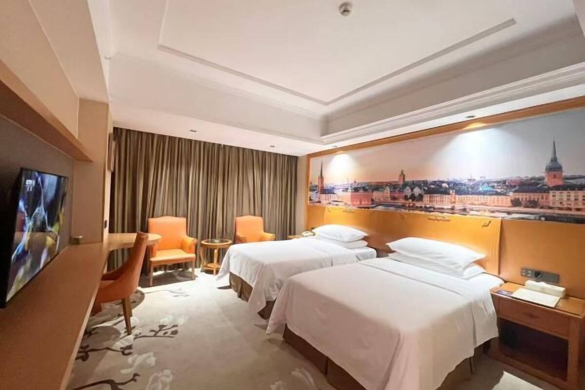 A hotel room with two beds, a TV, a painting of a cityscape, and a wooden headboard.