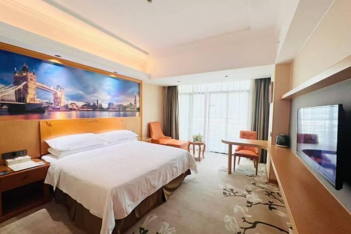A hotel room with a large bed, a desk, a chair, a television, and a painting of a cityscape.