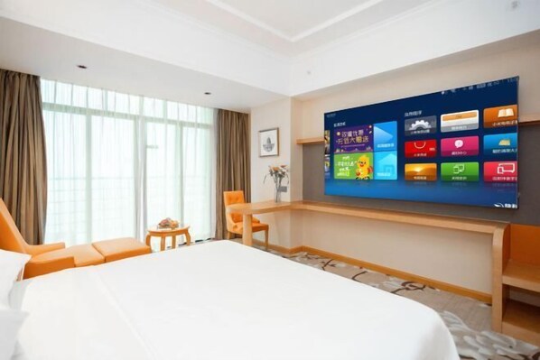 Ein Hotelzimmer mit einem großen Bett, einem an der Wand montierten Fernseher, der verschiedene Apps anzeigt, einem kleinen Tisch mit einer Vase und einem Fenster mit Vorhängen.