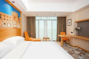 Ein Hotelzimmer mit einem Bett, zwei Stühlen, einem kleinen Tisch, einem Schreibtisch, einer Vase mit Blumen und einem großen Fenster mit Vorhängen.
