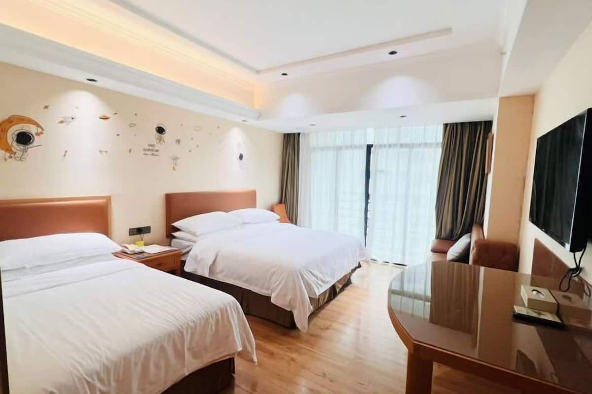 A hotel room with two beds, a flat-screen TV, a desk, and a large window with curtains.