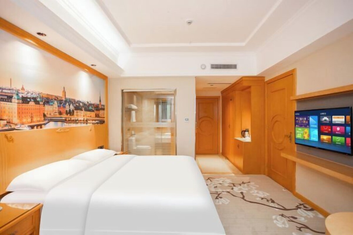 Ein Hotelzimmer mit einem Bett, einem Fernseher, Holztüren und einem Stadtbild-Wandgemälde.