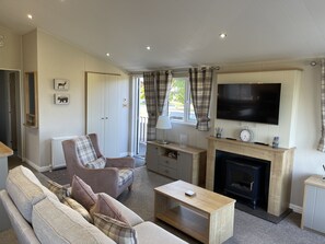 A living room with a sofa, armchair, fireplace, television, and a view of the outdoors. - Yorkshire view lodge (york)