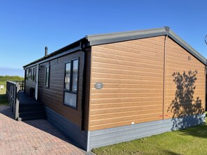 A modern building with a wooden exterior and a grey roof, featuring a staircase leading to a covered entrance. - Yorkshire view lodge (york)