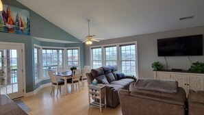 A spacious living room with a large window, a ceiling fan, and a flat-screen TV. - Belle Brísa-Canal front Surf City, NC (Surf City)