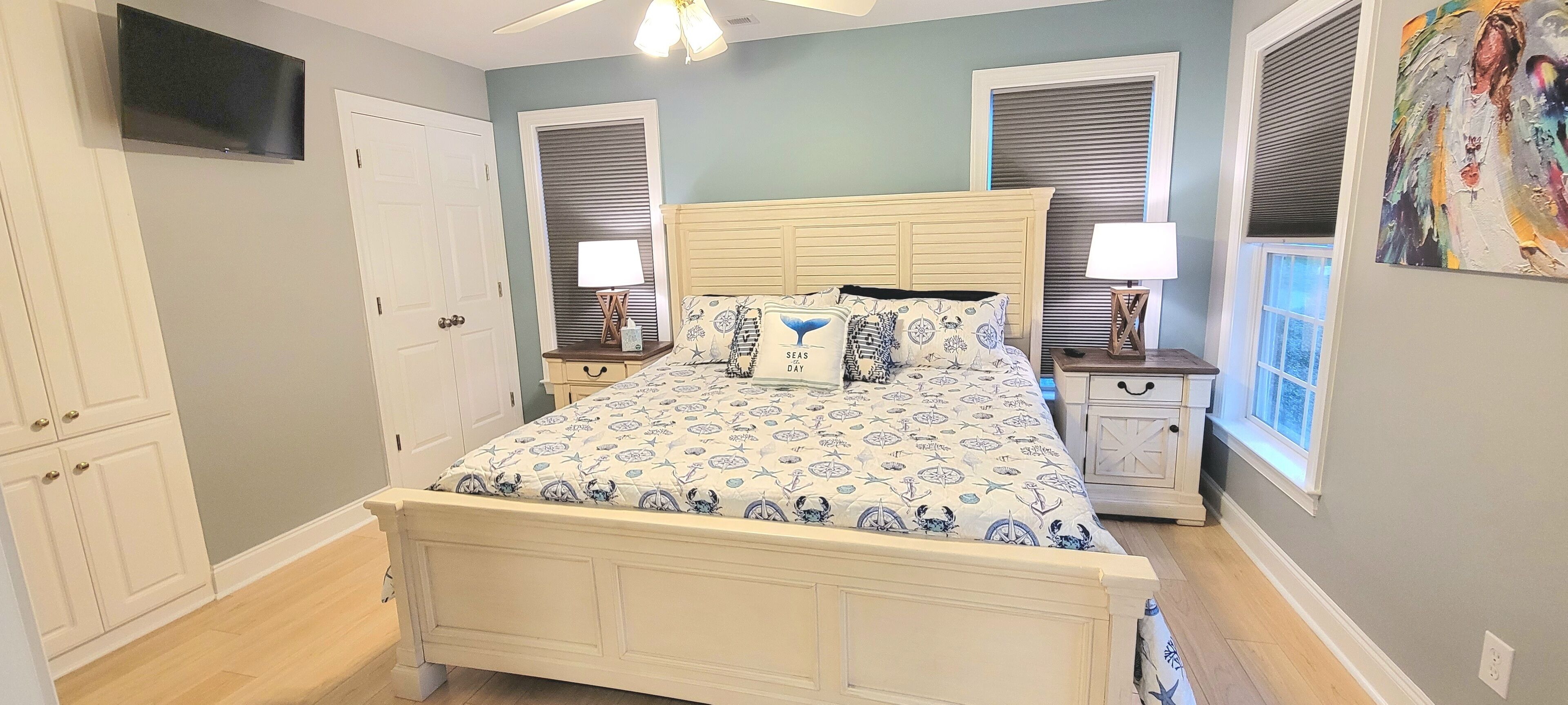 A bedroom with a bed, two bedside tables, a nightstand, a ceiling fan, a TV, and a window with blinds.