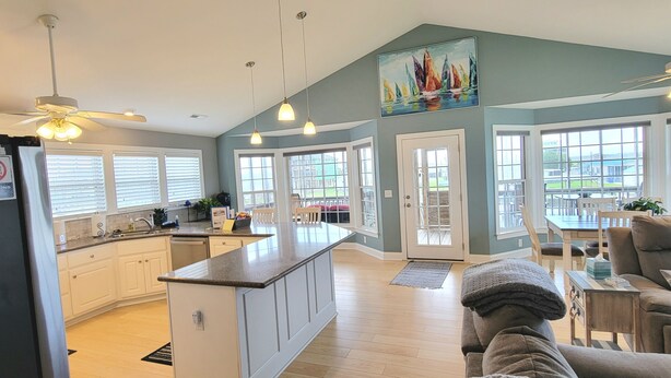 A spacious kitchen with a central island, a dining area with a table and chairs, and a living room with a sofa and a ceiling fan. - Belle Brísa-Canal front Surf City, NC (Surf City)