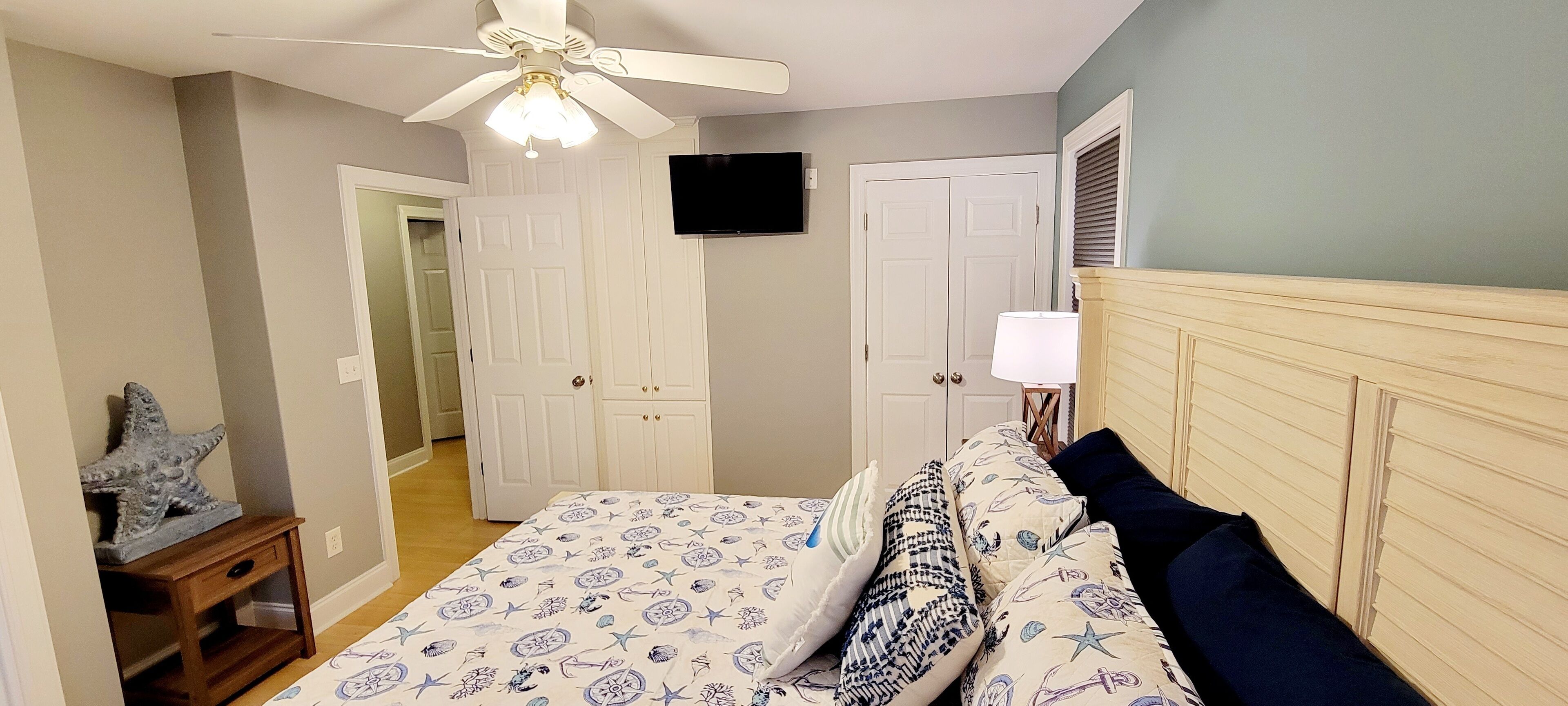 A bedroom with a bed, a ceiling fan, a TV, and a nightstand.