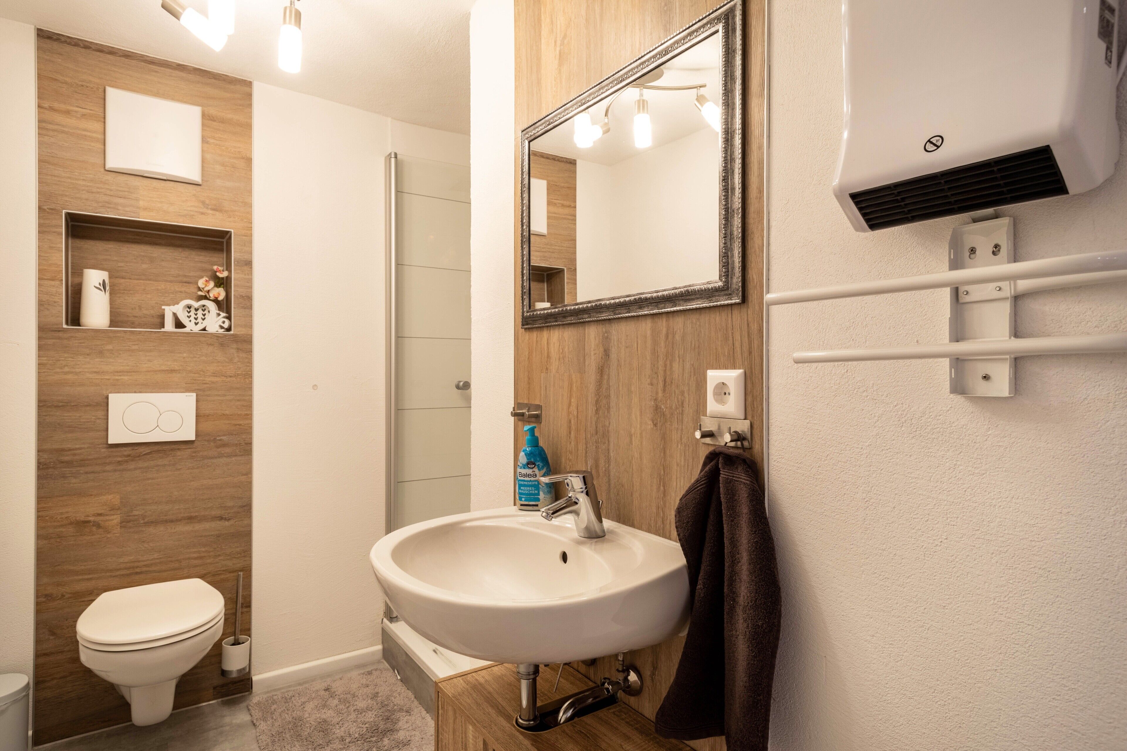 A bathroom with a white sink, a mirror, a towel rack, a shower, and a toilet.