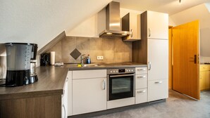 A modern kitchen with a built-in oven, a coffee maker, and a stainless steel range hood. - Holiday Apartment 'Nordsee Ferienwohnung Möwe' with Garden and Wi-Fi (Stedesdorf-Thunum)