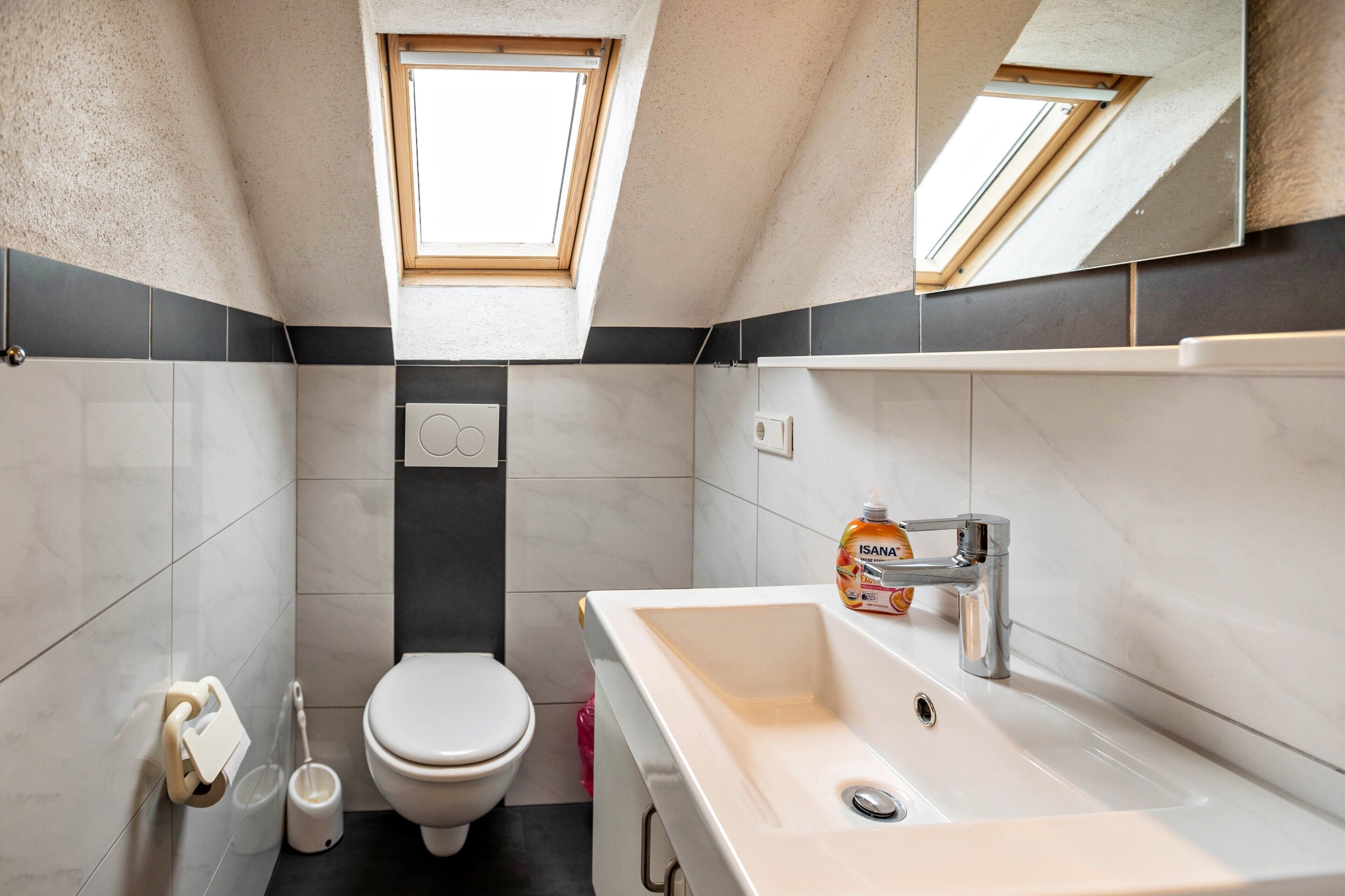 Een moderne badkamer met dakraam, toilet, wastafel en spiegel.