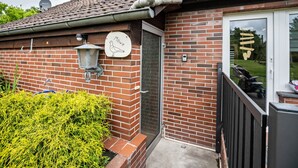 A brick building with a tiled roof, a door with a glass panel, a satellite dish, and a sign with a bird illustration. - Holiday Apartment 'Nordsee Ferienwohnung Möwe' with Garden and Wi-Fi (Stedesdorf-Thunum)