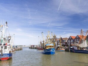Een haven met vissersboten die aanmeren, gebouwen met rode daken en een heldere lucht.