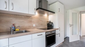A modern kitchen with a stainless steel sink, a built-in oven, and white cabinetry. - Apartment '9 und 40' with Garden and Wi-Fi (Stedesdorf-Thunum)