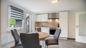 A modern kitchen with white cabinets, a round wooden table, and four chairs. - Apartment '9 und 40' with Garden and Wi-Fi (Stedesdorf-Thunum)
