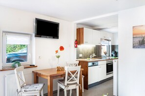 A modern kitchen with a built-in oven, a dishwasher, and a microwave. There is a dining area with a wooden table and two chairs. A flat-screen TV is mounted on the wall above the kitchen.