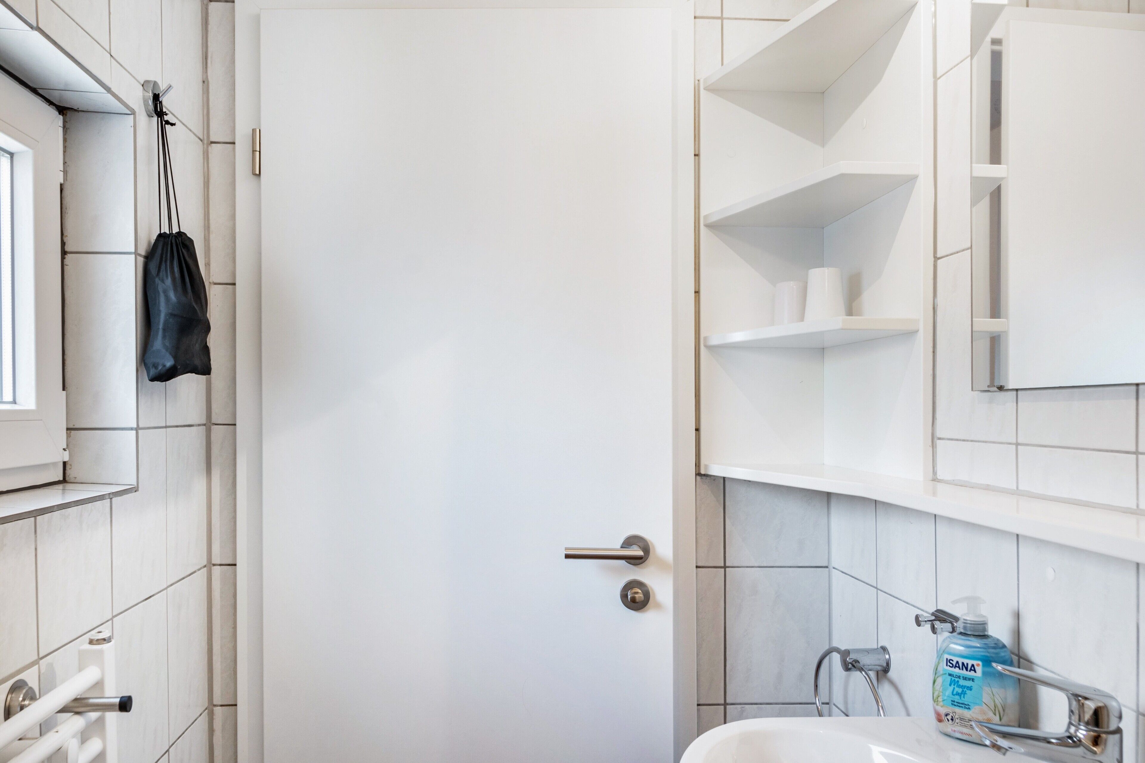 Een badkamer met een witte deur, een handdoekhouder, een wastafel met zeepdispenser en een spiegel boven een spiegelkast.