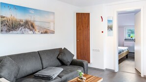 A modern living room with a grey sofa, a wooden coffee table, and a beach-themed painting on the wall.