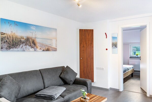 A modern living room with a grey sofa, a wooden coffee table, and a beach-themed painting on the wall.
