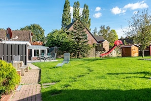 A backyard with a play area, a brick house, and a wooden deck.