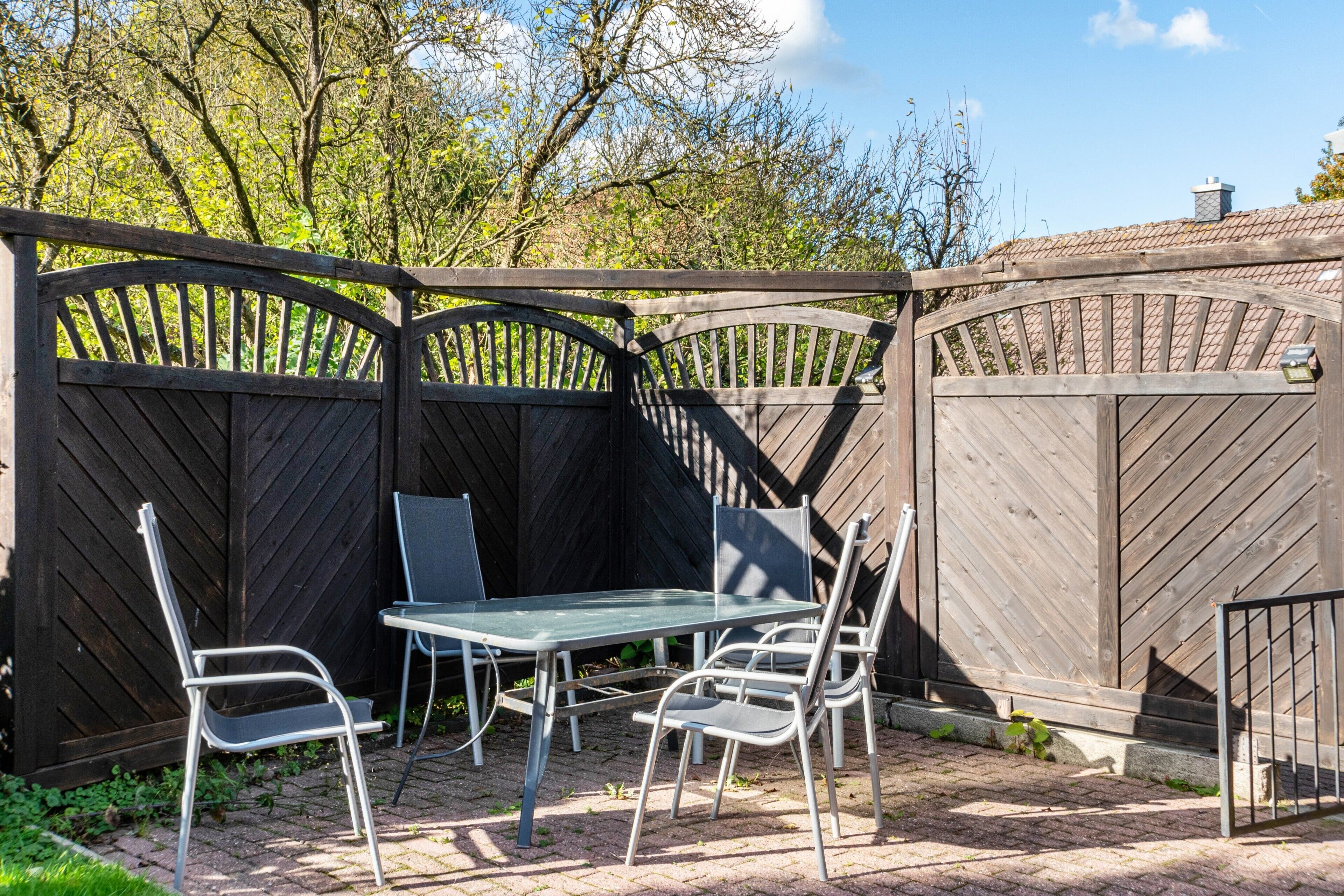 Une terrasse avec une table et des chaises, entourée d’une clôture en bois.