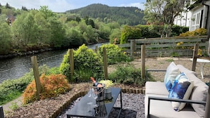 A terrace with a table, a sofa, and a view of a river and forest. - Coorie Doon, picturesque setting on Crinan Canal (Cairnbaan, Lochgilphead)