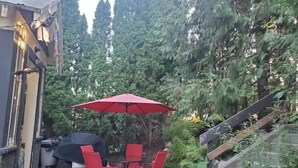 Een terras met een tafel, stoelen, een rode parasol en een barbecue.