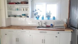 Een keuken met witte kasten, een houten aanrecht en een raam met planten.
