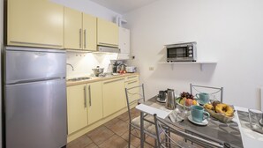 A compact kitchen with a refrigerator, microwave, and yellow cabinets. There is a dining table with chairs and a breakfast setting. - Casa Dolce Casa Central Stresa Apt 50m from lake, Stresa, Italy (Stresa)