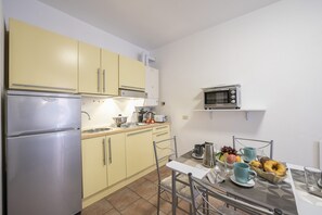 A compact kitchen with a refrigerator, microwave, and sink. There is a dining table with chairs and a breakfast setting.